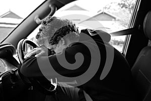 Sad and depressed mature adult man sitting in a car leaning on vehicle steering wheel