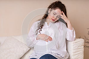 Sad, depressed pregnant woman suffering from headache, migraine, feeling sick, holding hand on head,