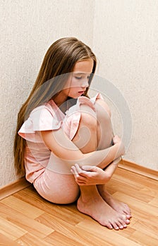 Sad and depressed punished little girl child sitting on the floor near the wall