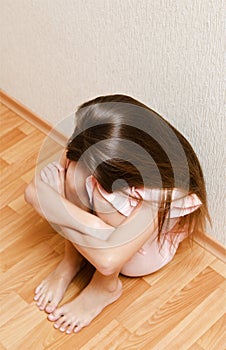 Sad and depressed punished little girl child sitting on the floor near the wall