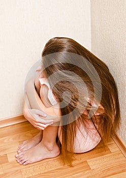 Sad and depressed punished little girl child sitting on the floor near the wall