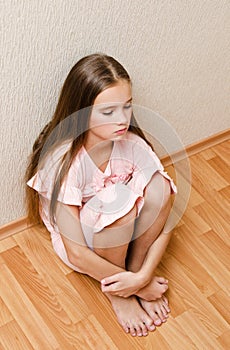 Sad and depressed punished little girl child sitting on the floor near the wall