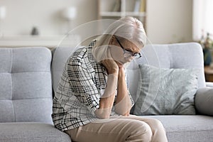 Sad depressed retired blonde woman sitting on sofa at home