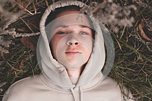 Sad and depressed teenager boy 16-18 year old wear hoody lying on ground outdoors. Autumn season. Teenagerhood. 20s