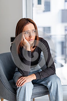 Sad depressed woman at home sitting on the couch, looking down and touching her forehead, loneliness and pain concept