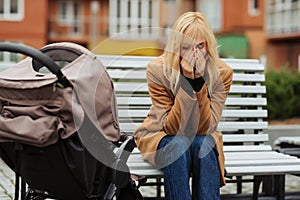 Sad and depressed woman sitting on a bench with her child in stroller.