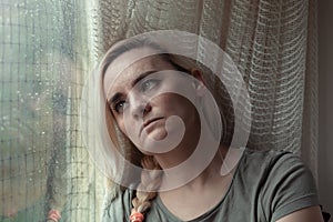 Sad, depressed woman sitting by the window, looking longingly out