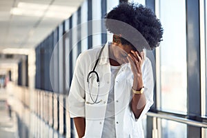 Sad and depressed young african american female doctor in white uniform standing in corridor