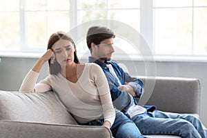 Sad depressed young caucasian wife ignores unhappy husband sitting on sofa in living room interior