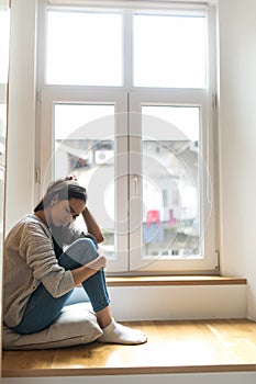 Sad depressed young woman having social problems sitting on windowsill