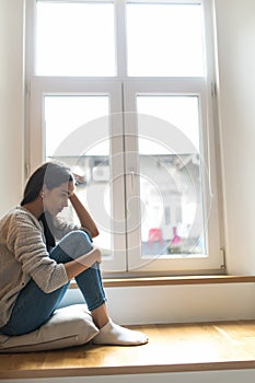 Sad depressed young woman having social problems sitting on windowsill