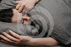 Sad depressed young woman lying on bed covering head with pillow feels unhappy and lonely, cheated unhappy girl suffers hurt