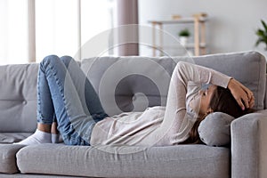 Sad depressed young woman lying on couch feeling headache