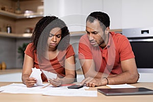 Sad despaired millennial black guy and lady, with tablet, pay bills and taxes together in kitchen interior