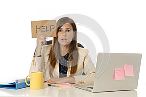 Sad desperate businesswoman in stress at office computer desk holding help sign