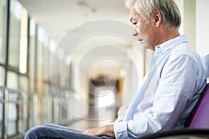 Sad and devastated asian old man sitting in hospital hallway photo