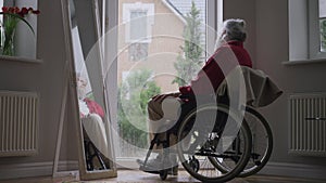 Sad disabled old man in wheelchair looking at rain out the window thinking. Wide shot of depressed hopeless Caucasian