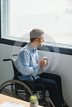 Sad disabled person feeling lonely at home or clinic. Depression on self isolation. Upset man in wheelchair looks out of