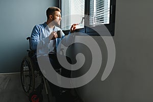 Sad disabled person feeling lonely at home or clinic. Depression on self isolation. Upset man in wheelchair looks out of