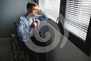 Sad disabled person feeling lonely at home or clinic. Depression on self isolation. Upset man in wheelchair looks out of