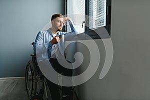 Sad disabled person feeling lonely at home or clinic. Depression on self isolation. Upset man in wheelchair looks out of