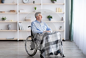 Sad disabled senior man sitting on wheelchair alone at retirement home, looking through window