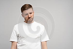 Sad disappointed man with head down on gray background. Portrait of young upset frustrated guy.