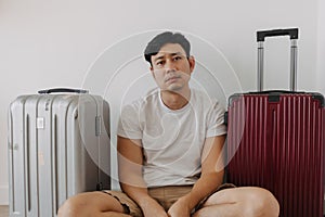 Sad disappointed man sit with his luggages as his traveling trip plan has been cancelled.