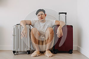 Sad disappointed man sit with his luggages as his traveling trip plan has been cancelled.