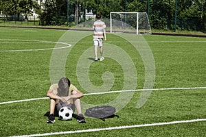 Sad disappointed teenage boy sitting in empty school sport stadium outdoors. Friend walks away and leaves his friend