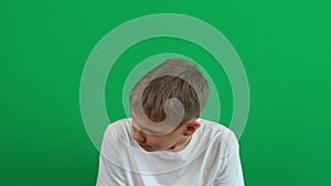 Sad disappointed teenage boy sitting and shaking his lowered head in despair. Green screen chroma key background. 4k