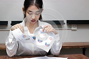 Sad and disappointed young Asian business woman tearing charts or document paper in office. Bad investment crisis concept