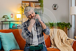 Sad disinterested senior man talking on vintage retro wired telephone with hotline helpline service