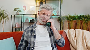 Sad disinterested senior man talking on vintage retro wired telephone with hotline helpline service