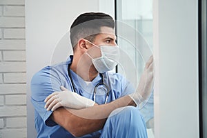 Sad doctor near window indoors. Stress of health care workers during coronavirus pandemic