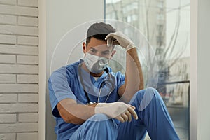 Sad doctor near window indoors. Stress of health care workers during coronavirus pandemic