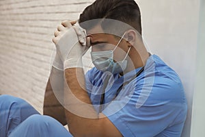 Sad doctor near window, view from outdoors. Stress of health care workers during coronavirus pandemic