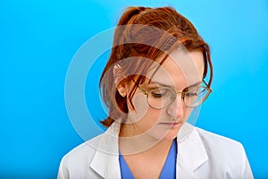 Sad doctor in a white medical coat, blue background. Close-up nurse with red hair. Stay home concept