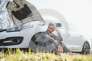 Sad driver holding his head having engine problem standing near broken car on the road. Car breakdown concept