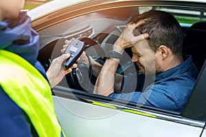sad drunk man sitting in the car after police alcohol test with alcometer