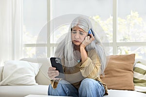 Sad elderly Hispanic woman looking at phone and credit card