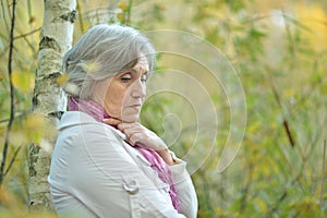 Sad elderly woma standing by a tree