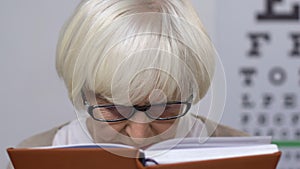 Sad elderly woman in eyeglasses reading book, vision problems, blindness