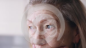 Sad elderly woman looking through the window. Depression and anxiety at old age. Close up