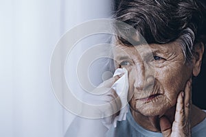 Sad elderly woman wiping tears