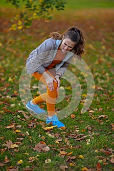 sad elegant woman in fitness clothes in park having leg pain