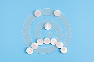 Sad emoticon from medical pills on a blue background