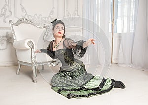 Sad emotional woman wearing green medieval vintage Victorian Style dress sitting on the floor