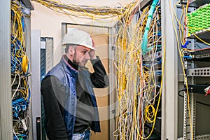 A sad engineer in a white helmet took his head in the server room. The specialist sees problems with cable management in the