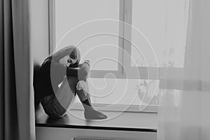 Sad exhausted woman sitting next to the window lonely and tired